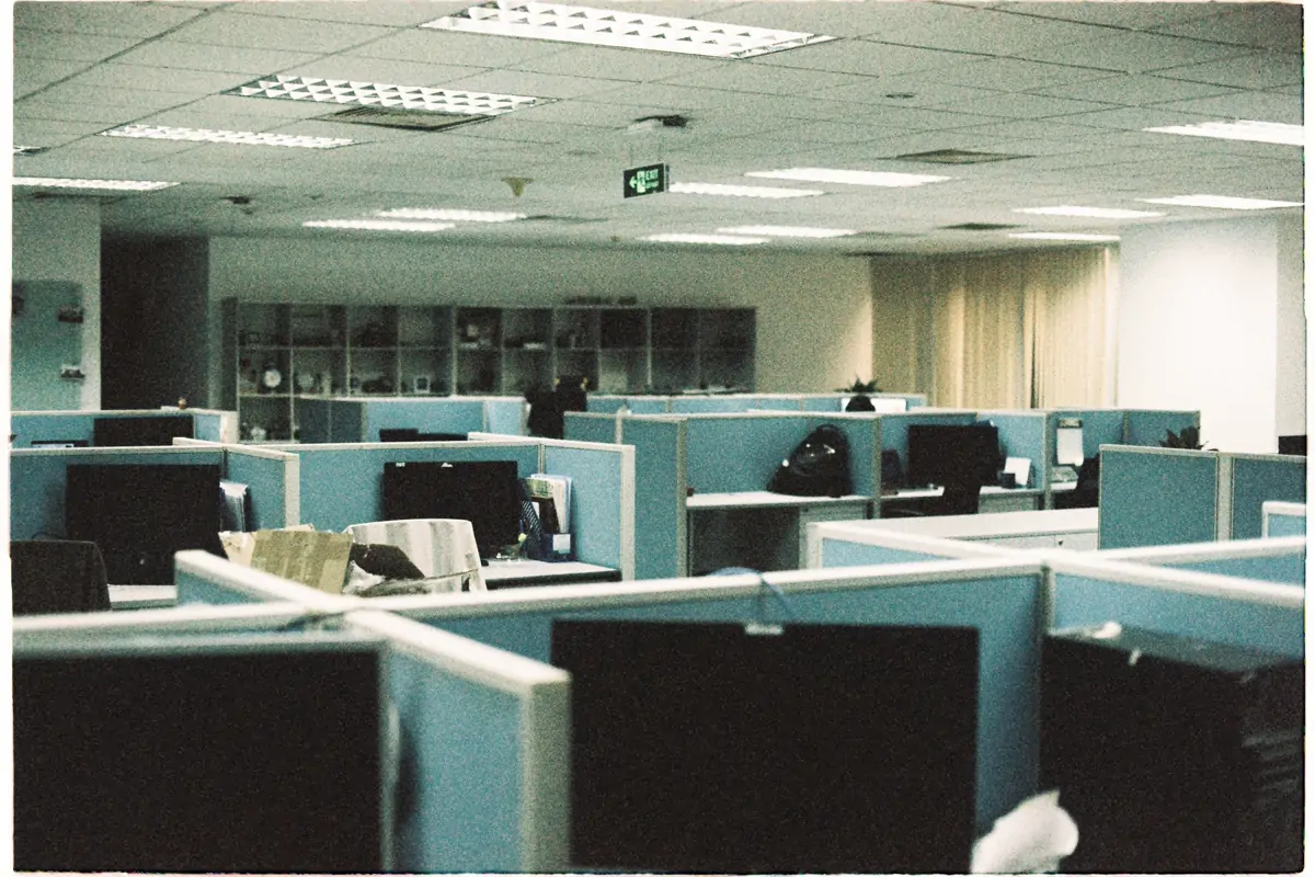 Rows of empty office cubicles with computer monitors under ceiling lights