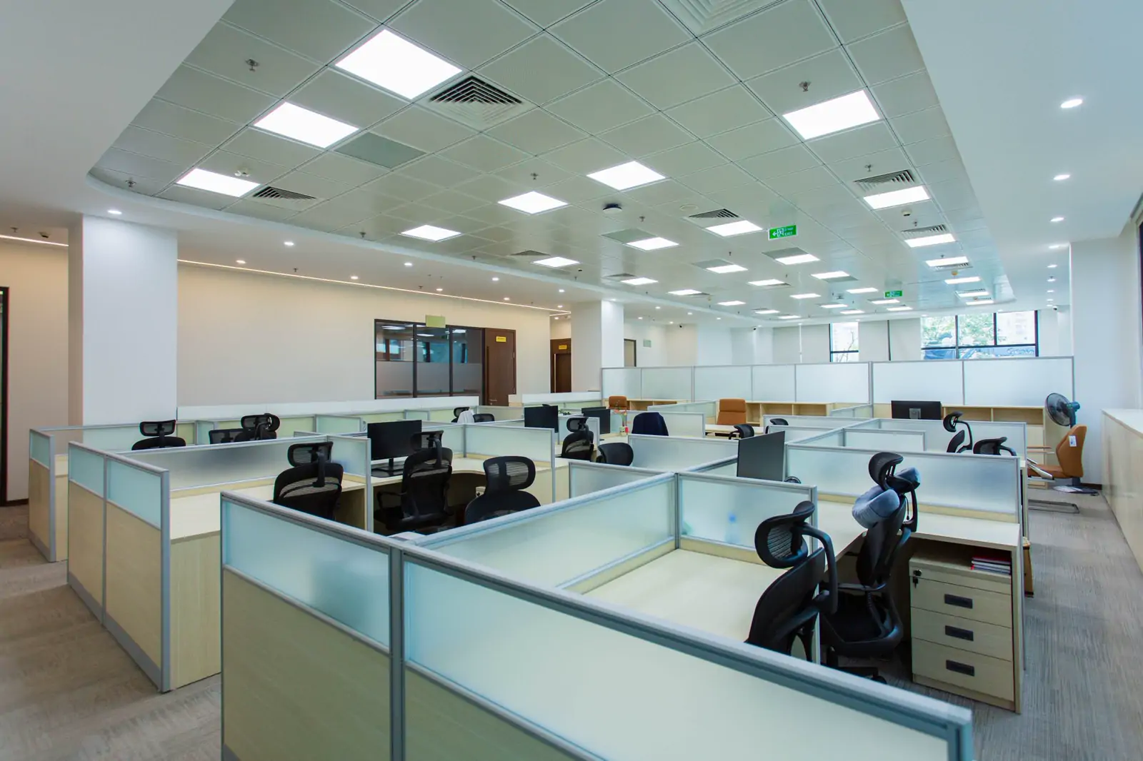A bright open-plan office with rows of workstations divided by low glass partitions