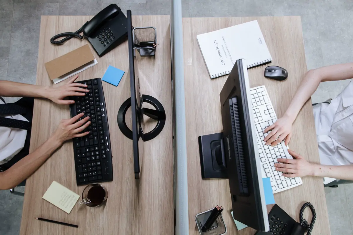 Two office workstations seen from directly above, with people typing at keyboards