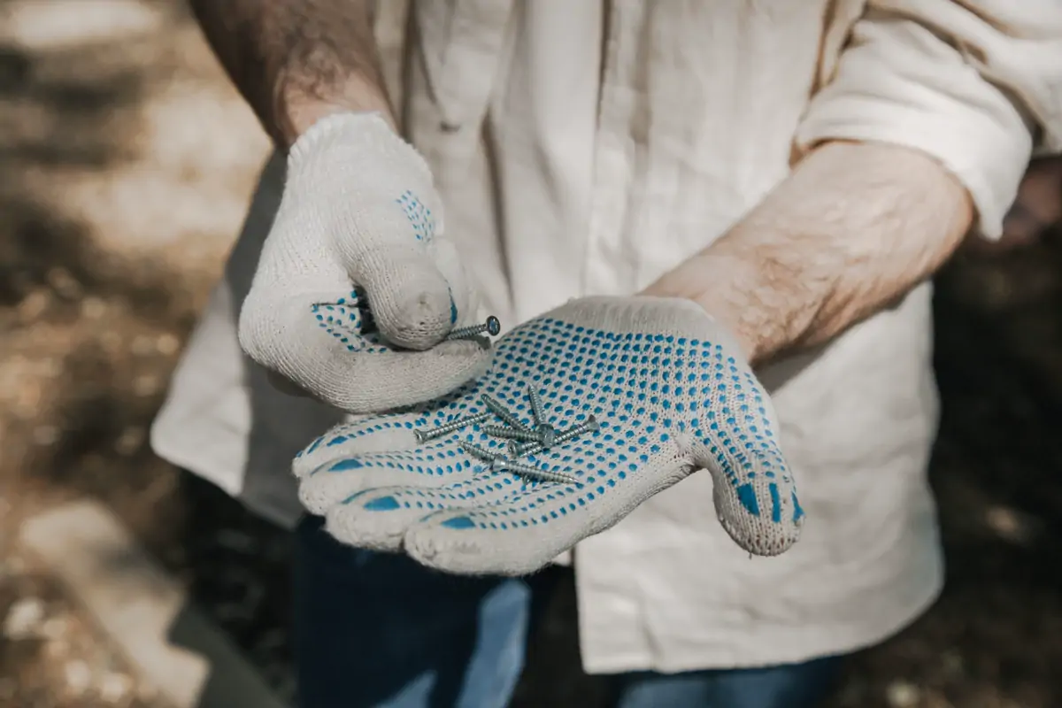 Hands in knitted safety gloves holding a few small screws