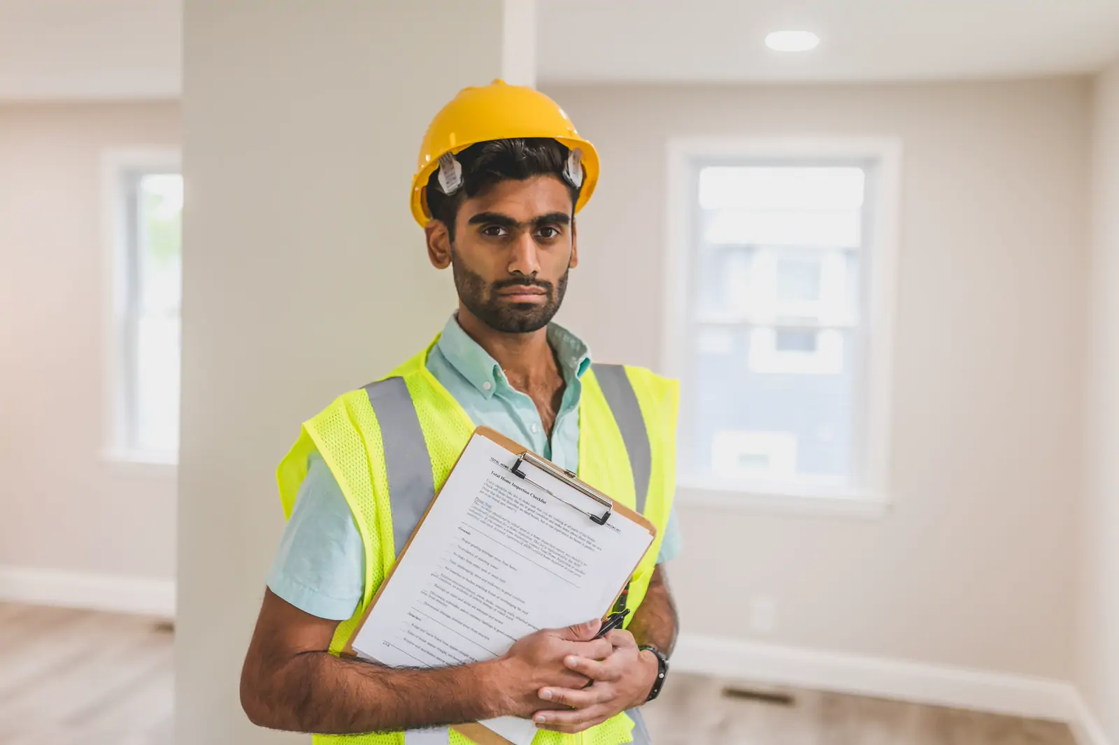 A site supervisor in a yellow safety helmet and high-visibility vest holding a clipboard