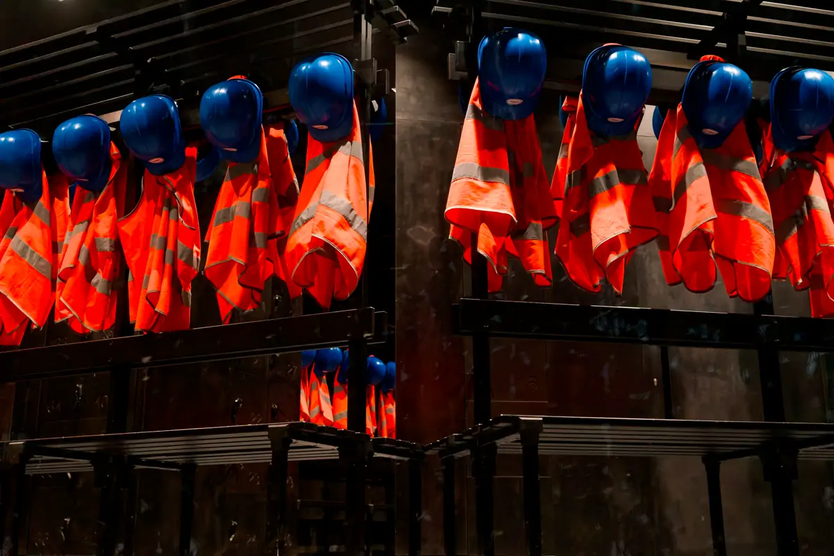 Orange high-visibility vests and blue safety helmets hanging on a rack